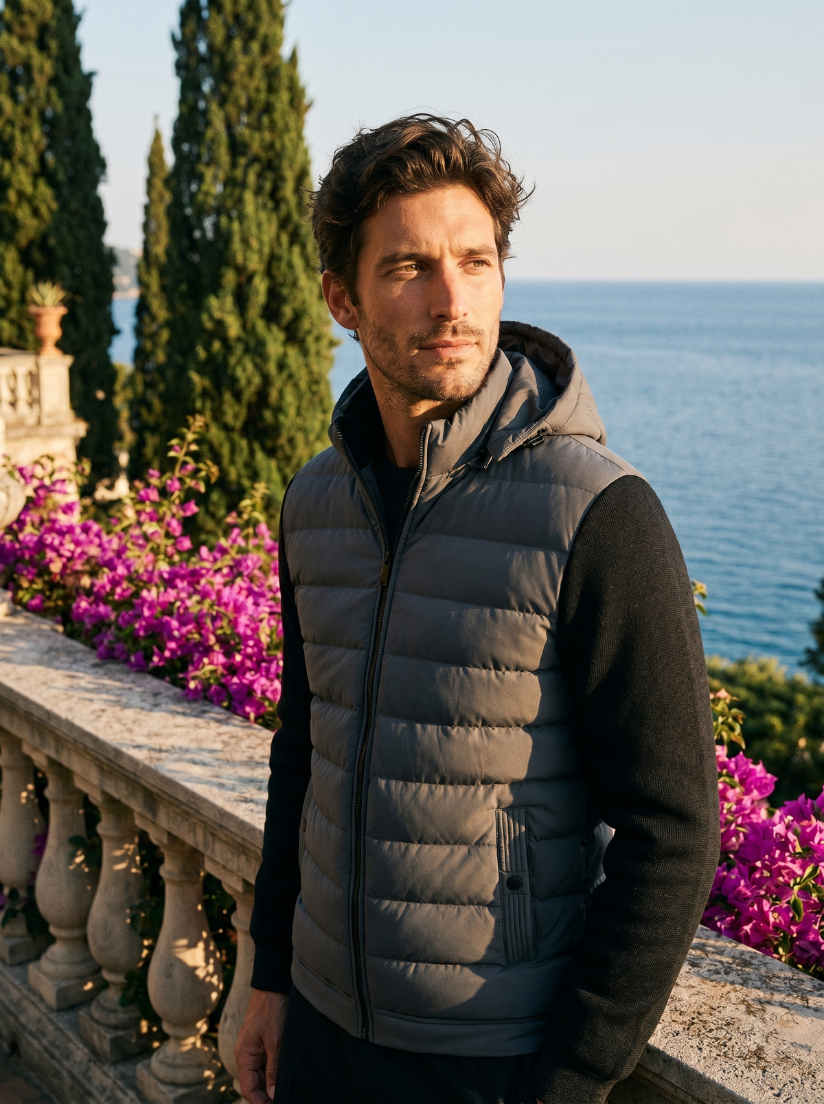 Man wearing a grey hooded puffer jacket on a balcony overlooking Lake Como, old money style — Belvoirne