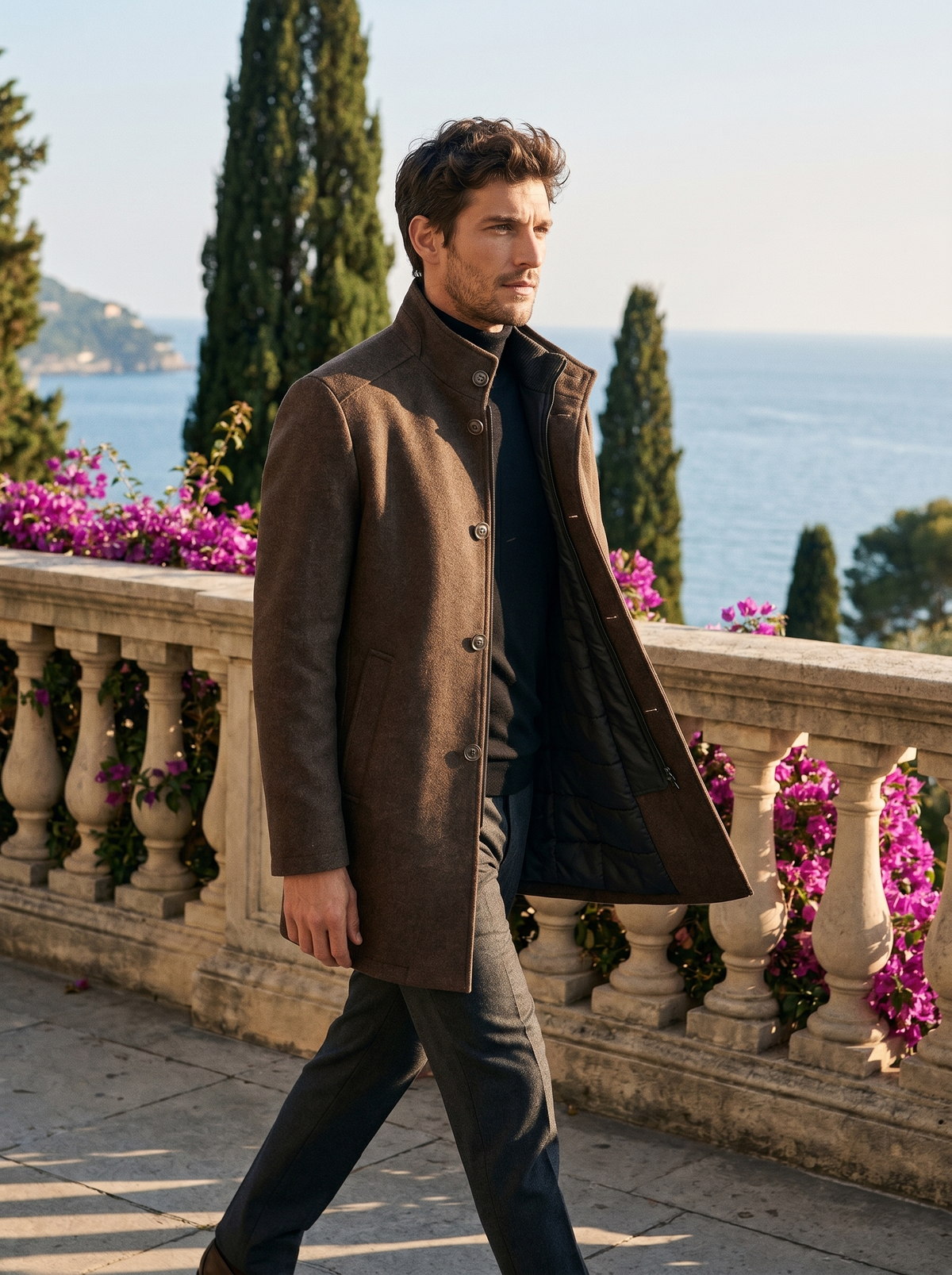 Full-length shot of a man walking in a brown stand-collar tailored coat by Lake Como — Belvoirne